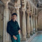 A South Asian man poses against ornate stone columns in an Indian palace.